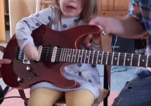 dziewczynka trzyma gitarę i na niej gra